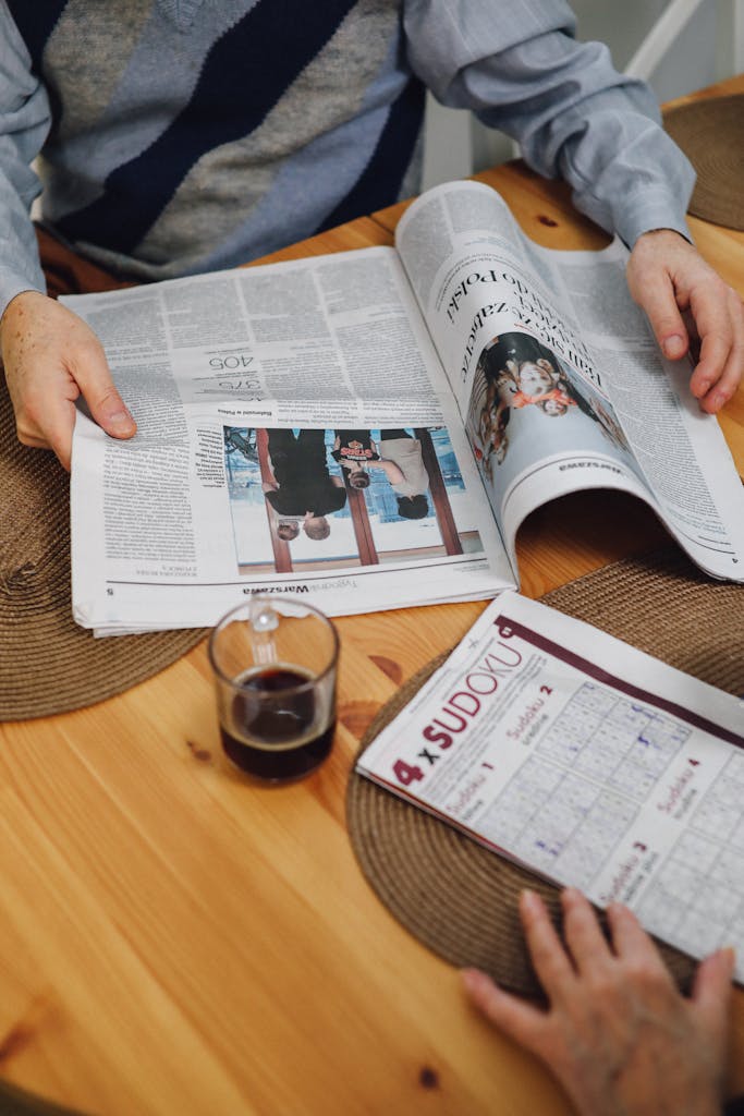 High-angle view of senior adults reading a newspaper with coffee on a wooden table.